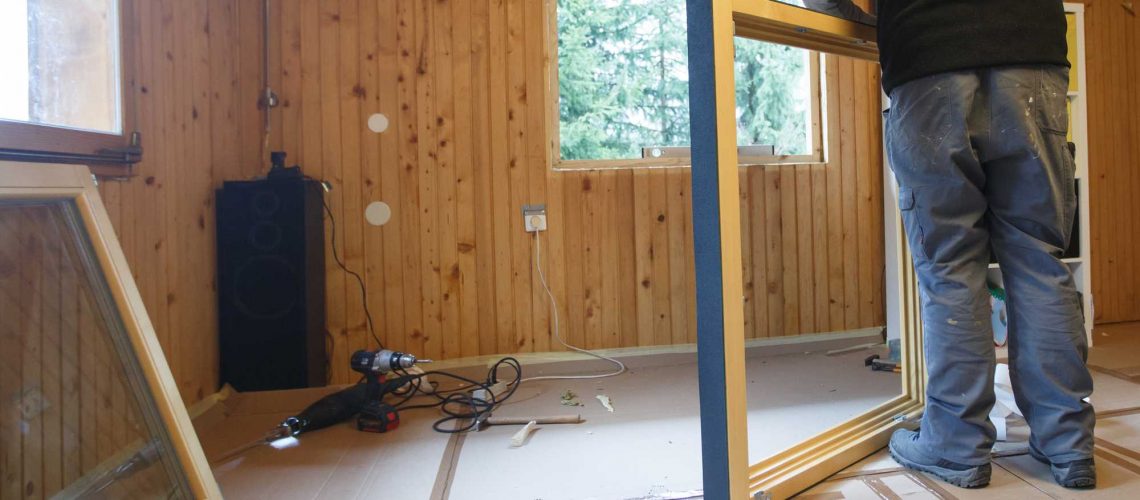 Worker preparing to install new three pane wooden windows in an old wooden house. Home renovation, sustainable living, energy efficiency concept.