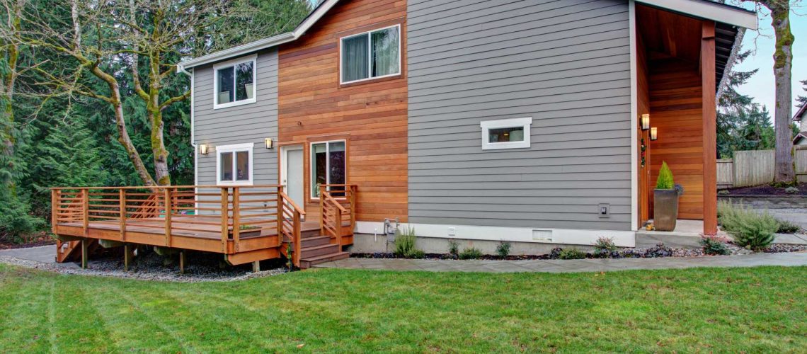 Charming newly renovated home exterior, natural wood siding and grey siding create a beautiful curb appeal. View of a nice walk out deck with wooden handrails.